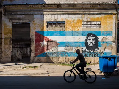 A cyclist rides past a colorful mural, featuring the Cuban flag and an image of Guevara.
&nbsp;