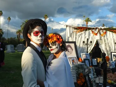 A couple visits a cemetery during Day of the Dead, against the backdrop of storm clouds.