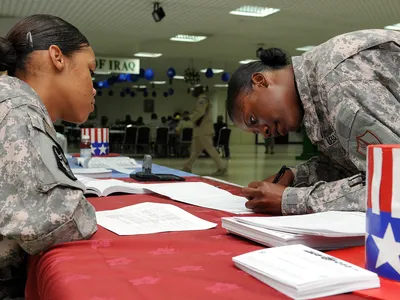 U.S. Army Pfc. Chyna Williams (left) helps Staff Sgt. Janeen Butler at a voter assistance drive on a base in Qatar, 2008